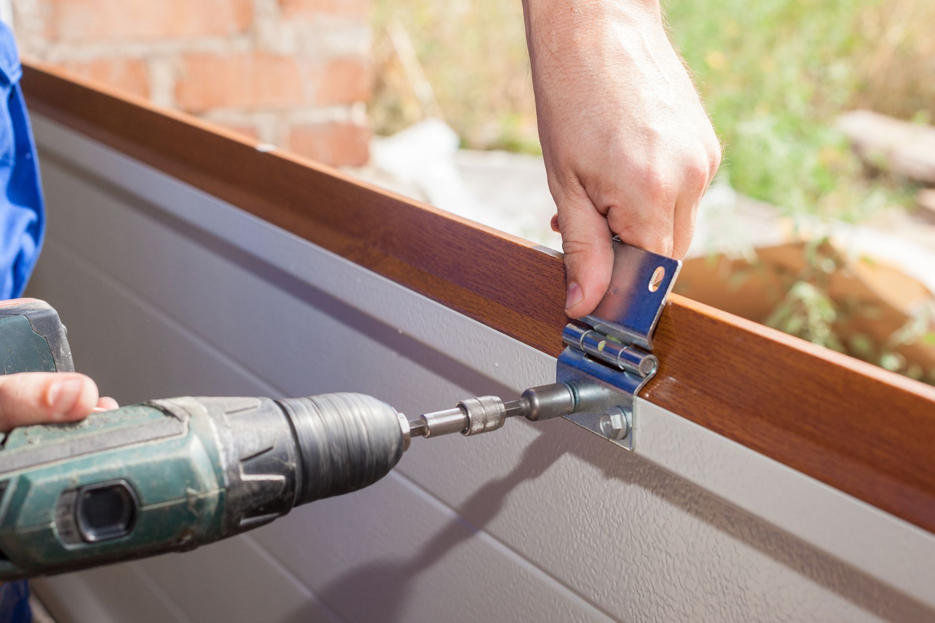 Fixing and replacement concept. Cropped view of professional worker using electric screwdriver and install new garage door system in house under construction.