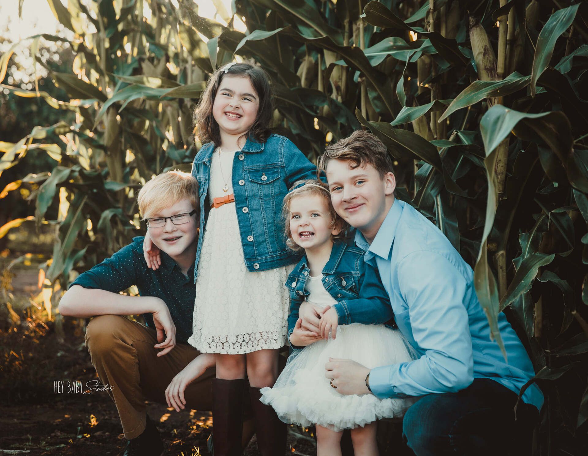 A group of children are posing for a picture in a corn field.