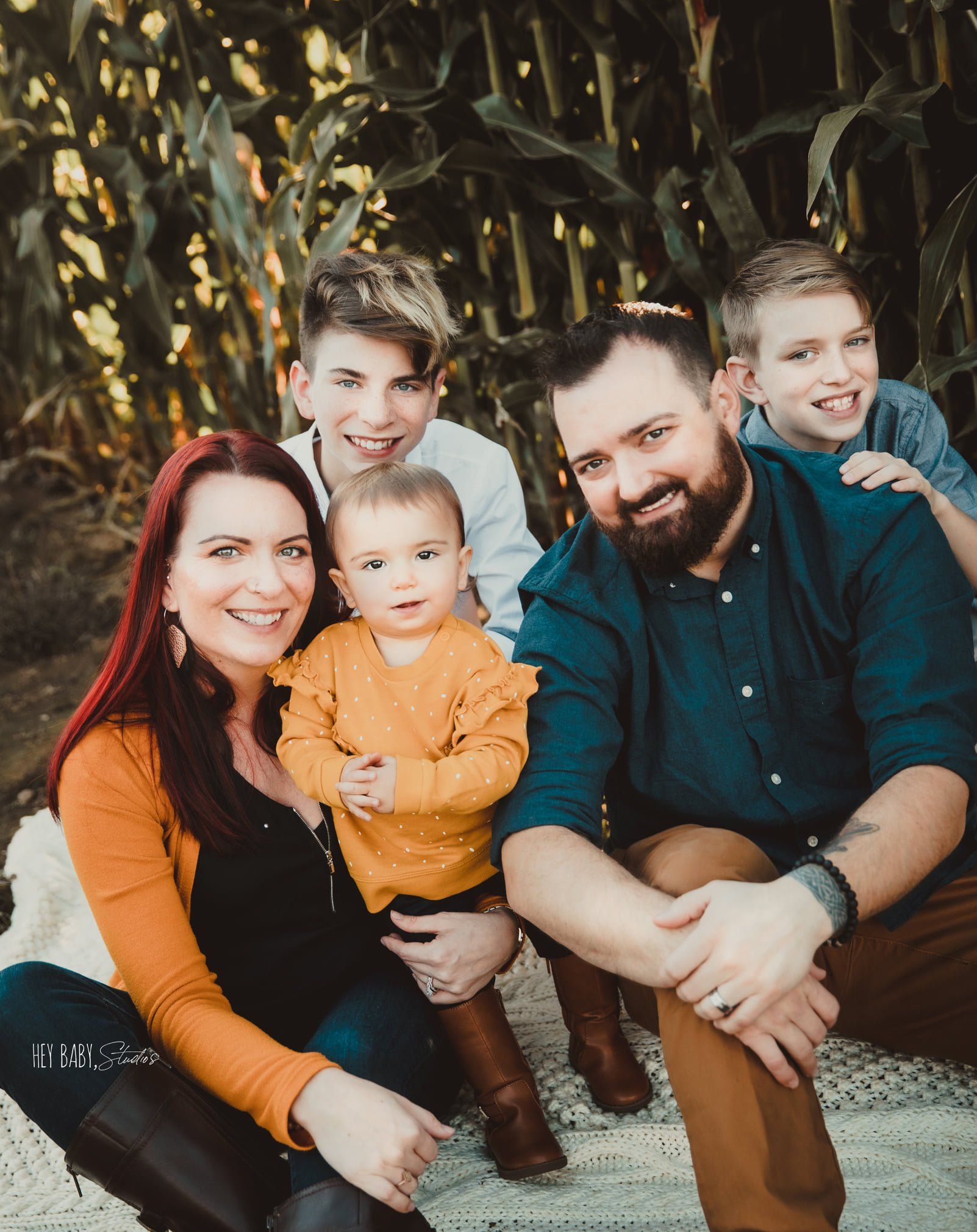 A family is posing for a picture in front of a corn field.