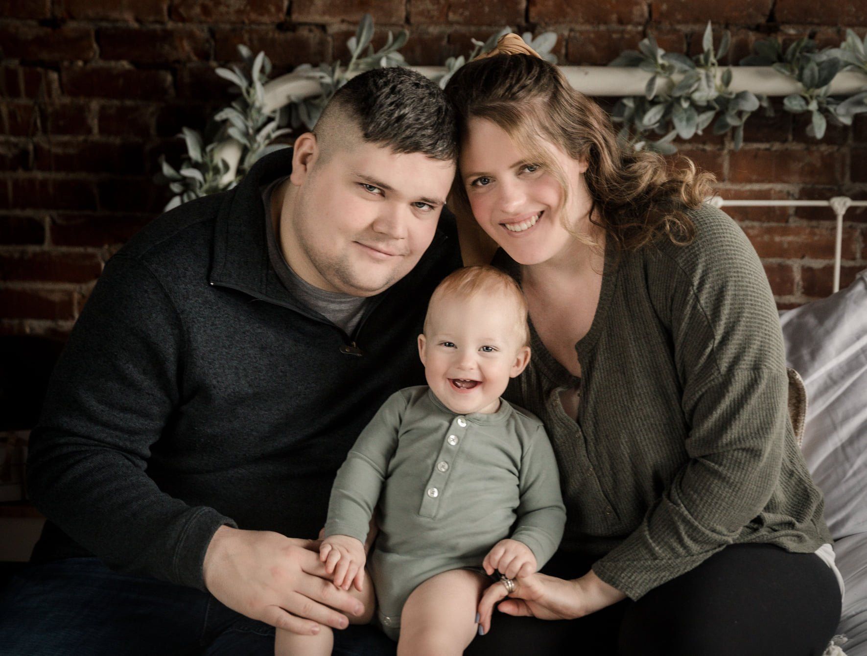 A man and woman are sitting on a bed with a baby.