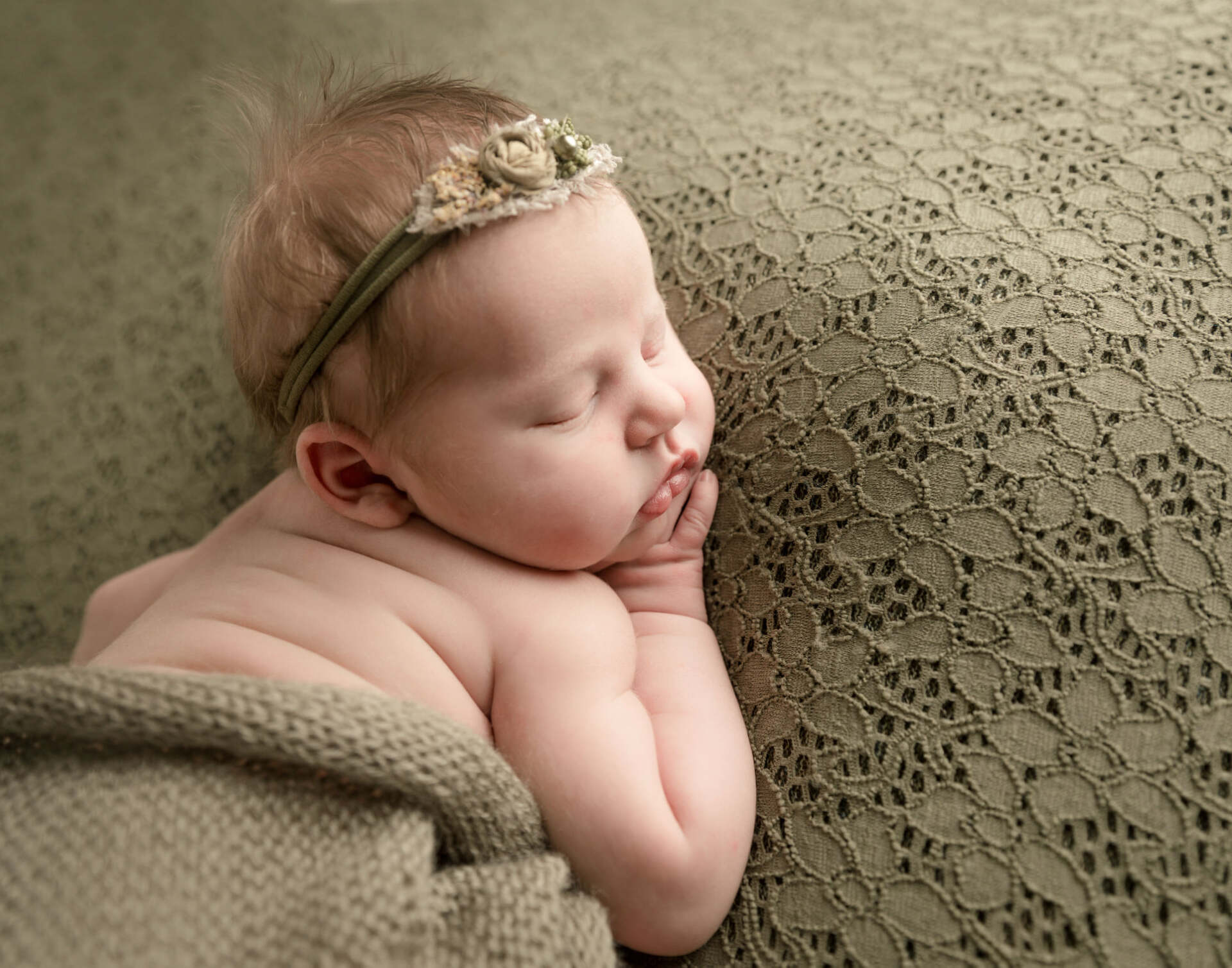 A newborn baby girl wearing a headband is sleeping on a blanket.