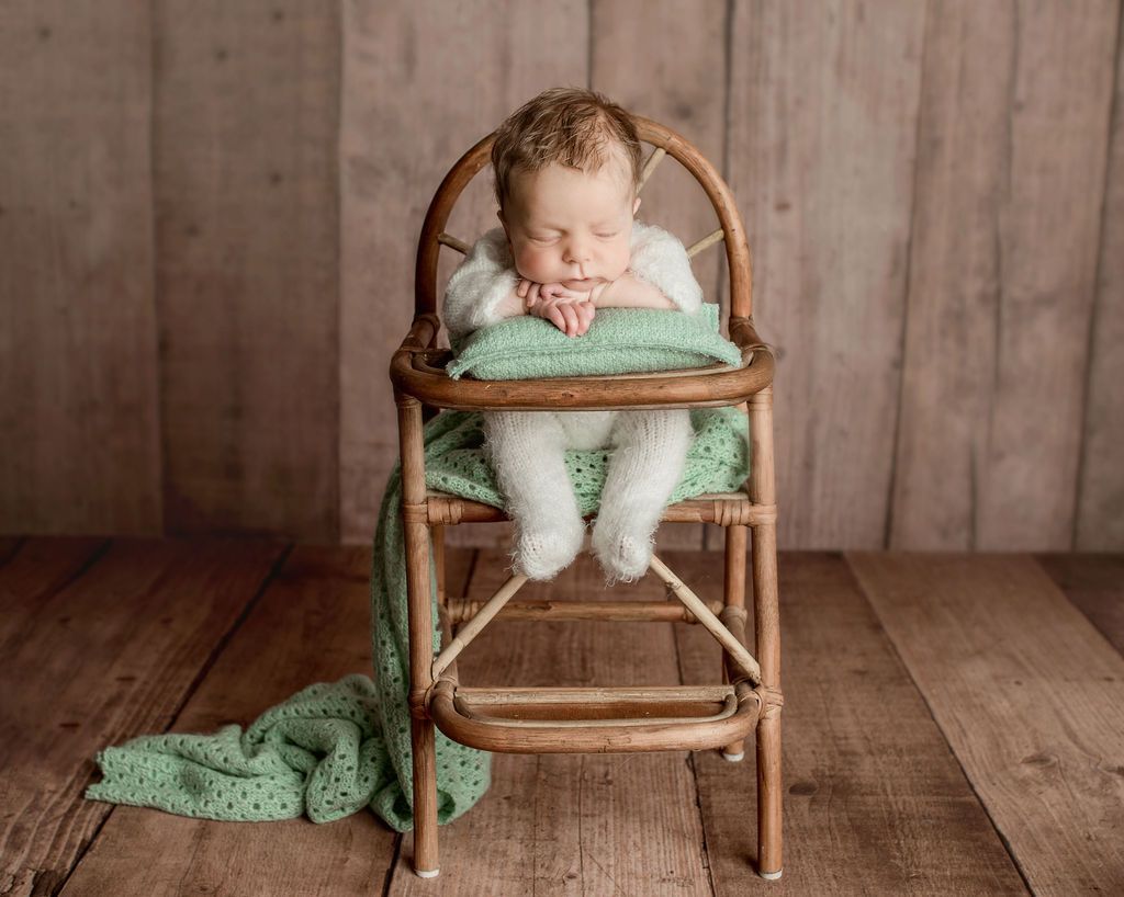 A newborn baby is sleeping in a wooden high chair. Baby Props