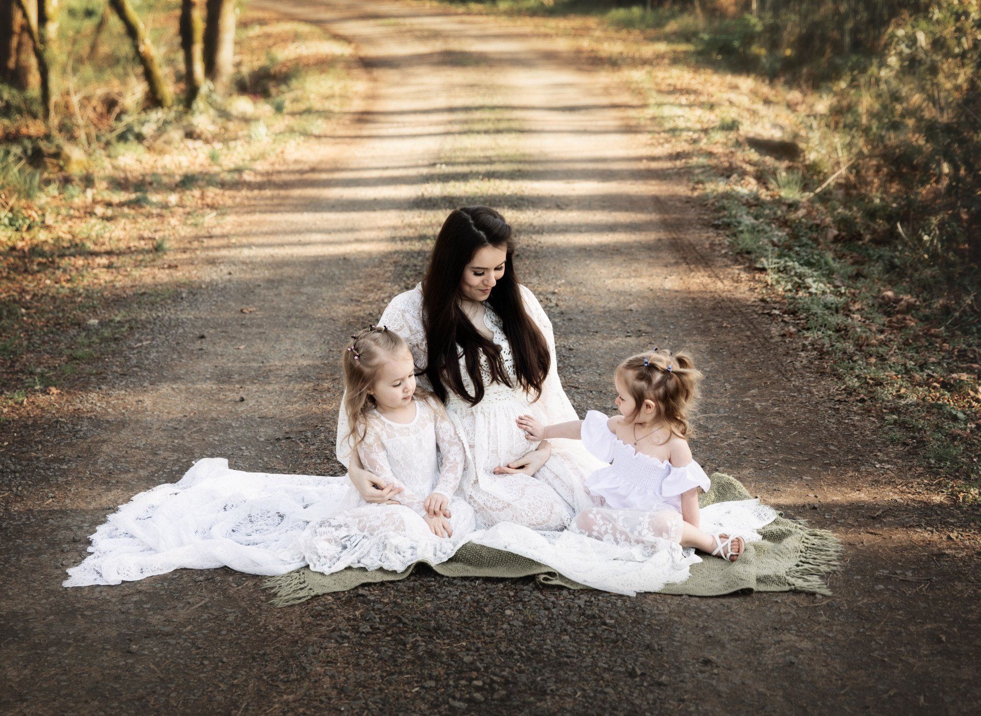 A pregnant woman is sitting on the ground with two little girls. Maternity Photos.