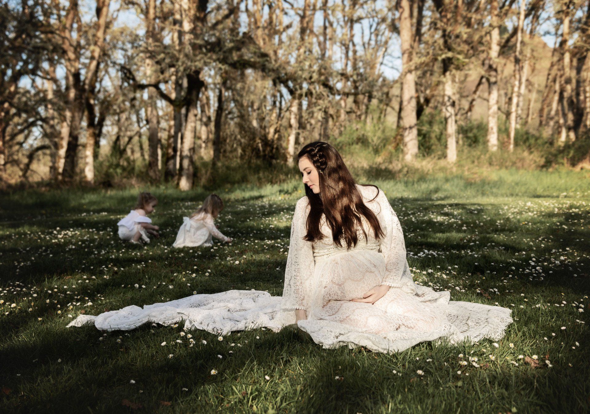 A woman in a white dress is sitting in the grass with two children.