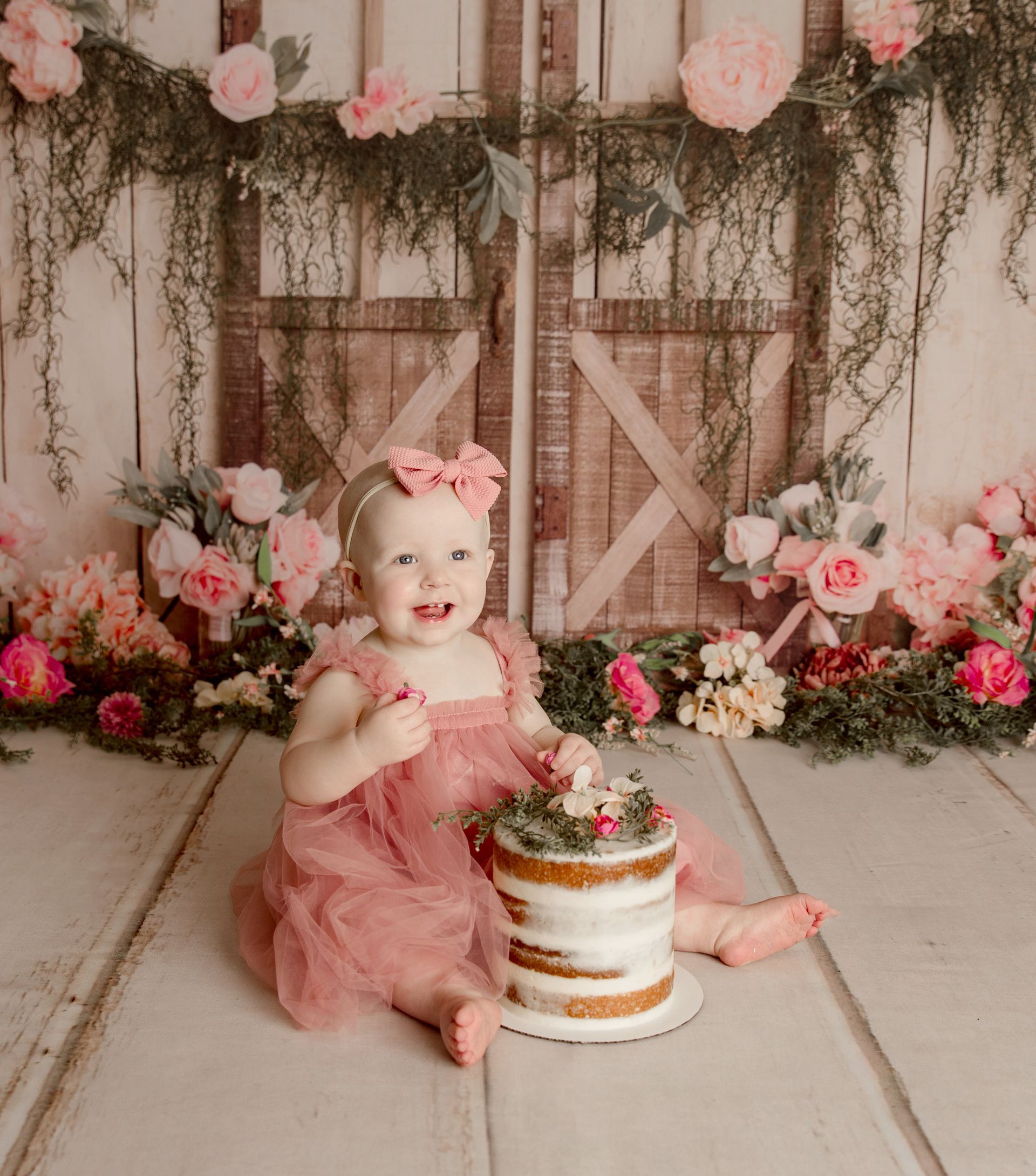 A baby girl is sitting on a wooden floor next to a cake.