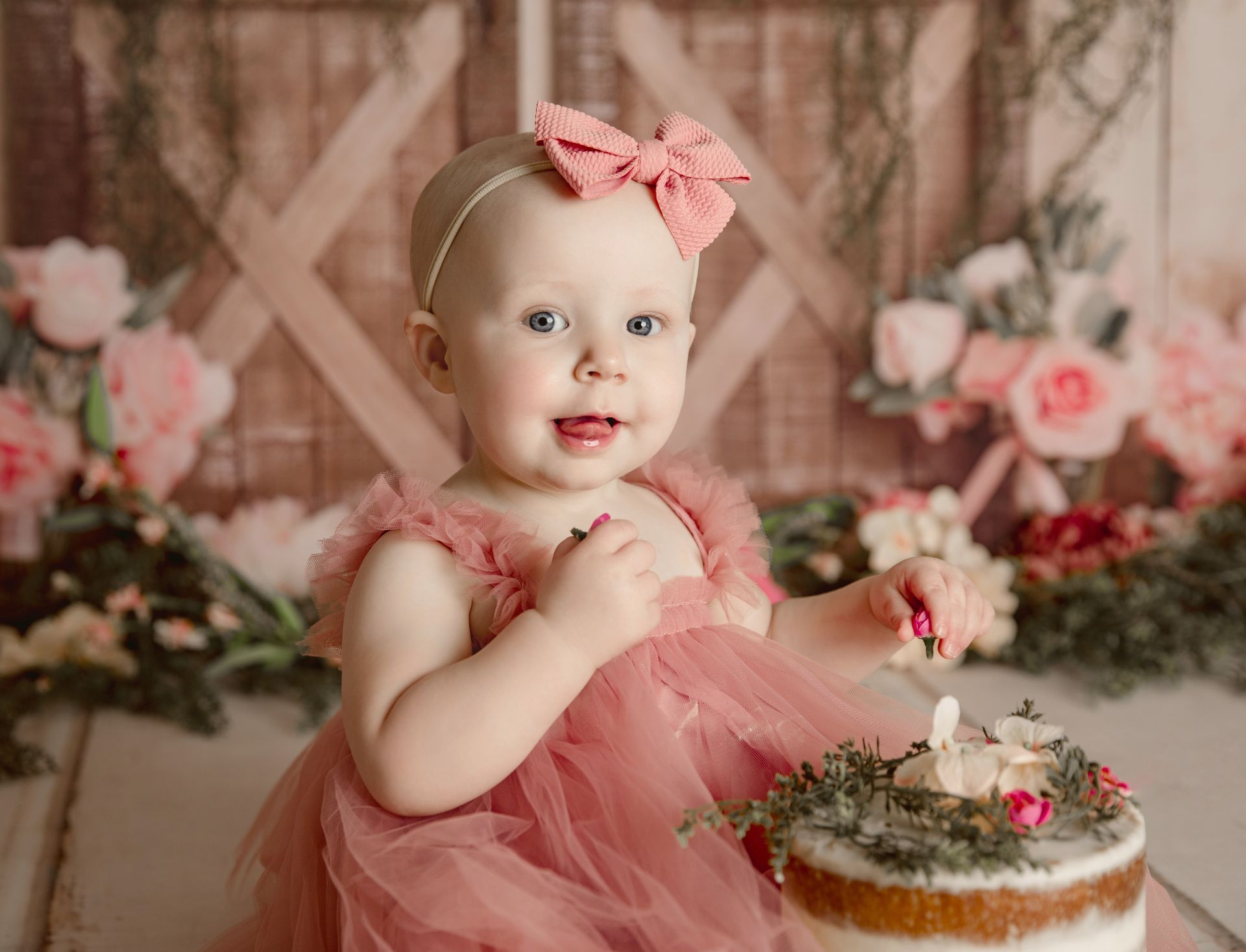 A baby girl in a pink dress is sitting next to a cake.