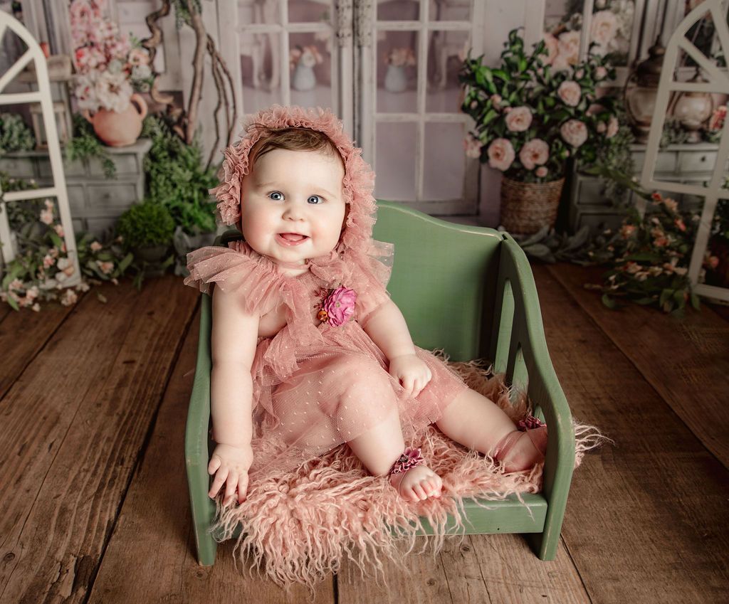A baby in a pink dress is sitting in a green crib.