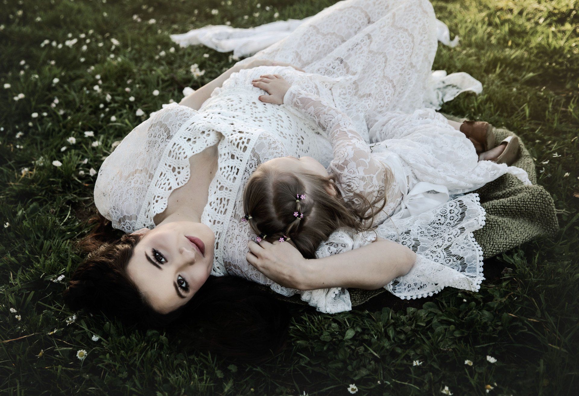 A pregnant woman and a little girl are laying in the grass.