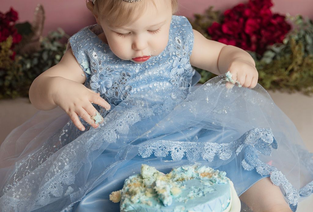A little girl in a blue dress is eating a blue cake.