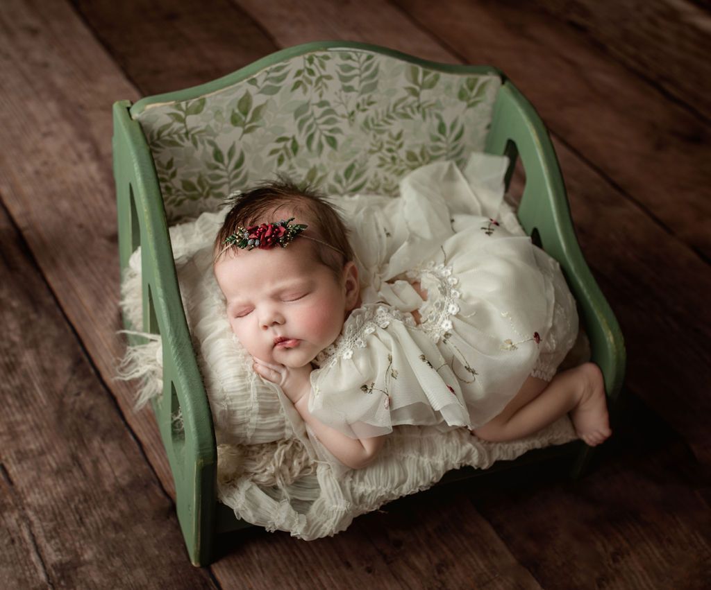A newborn baby in a white dress is sleeping in a green crib. Baby Studio with Props