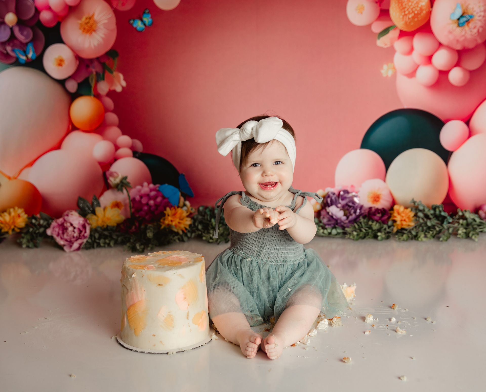 A baby girl is sitting on the floor next to a cake.