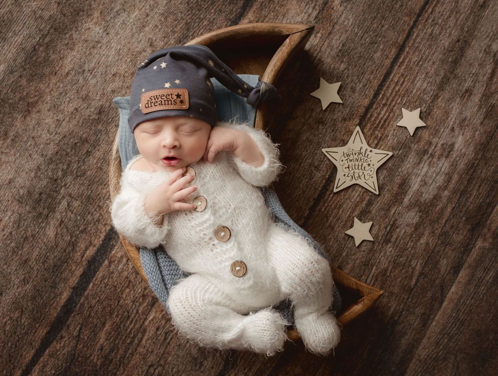 A newborn baby is sleeping in a basket on a wooden floor.
