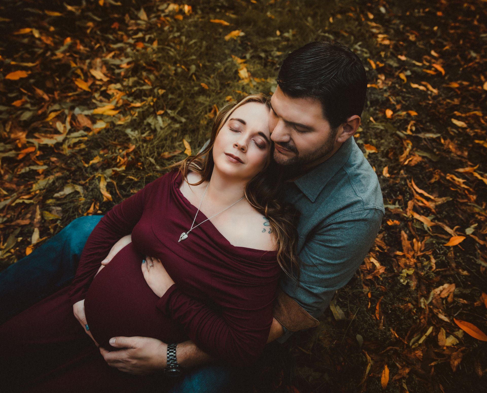 A pregnant woman is laying on a man 's lap in the grass.