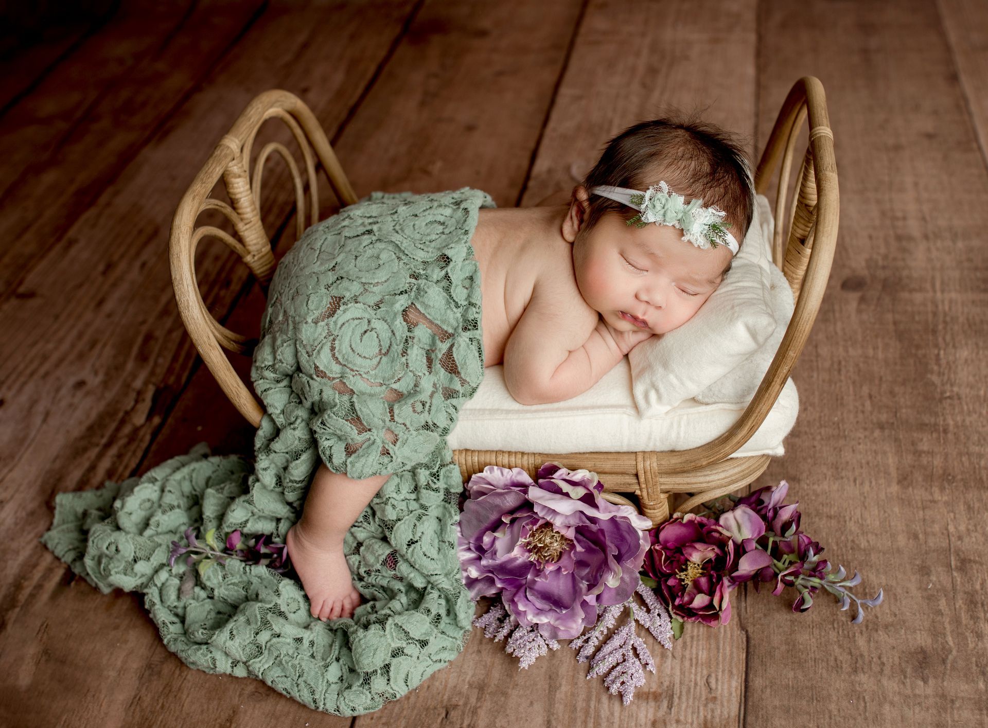 A newborn baby is sleeping in a wicker bed with flowers.