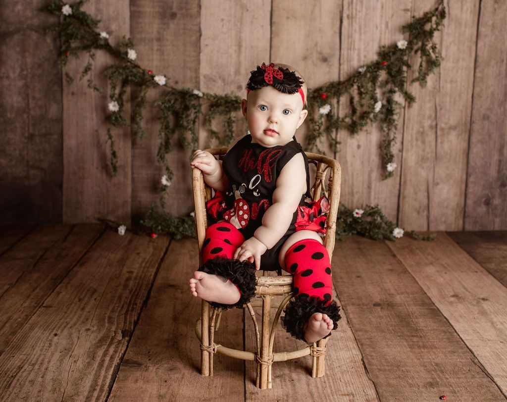 A baby girl is sitting in a chair wearing a ladybug outfit.