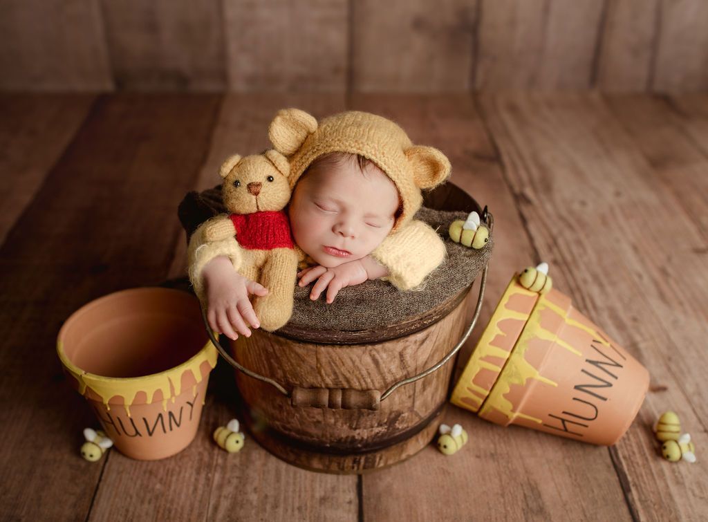 A newborn baby dressed as winnie the pooh is sleeping in a wooden bucket.