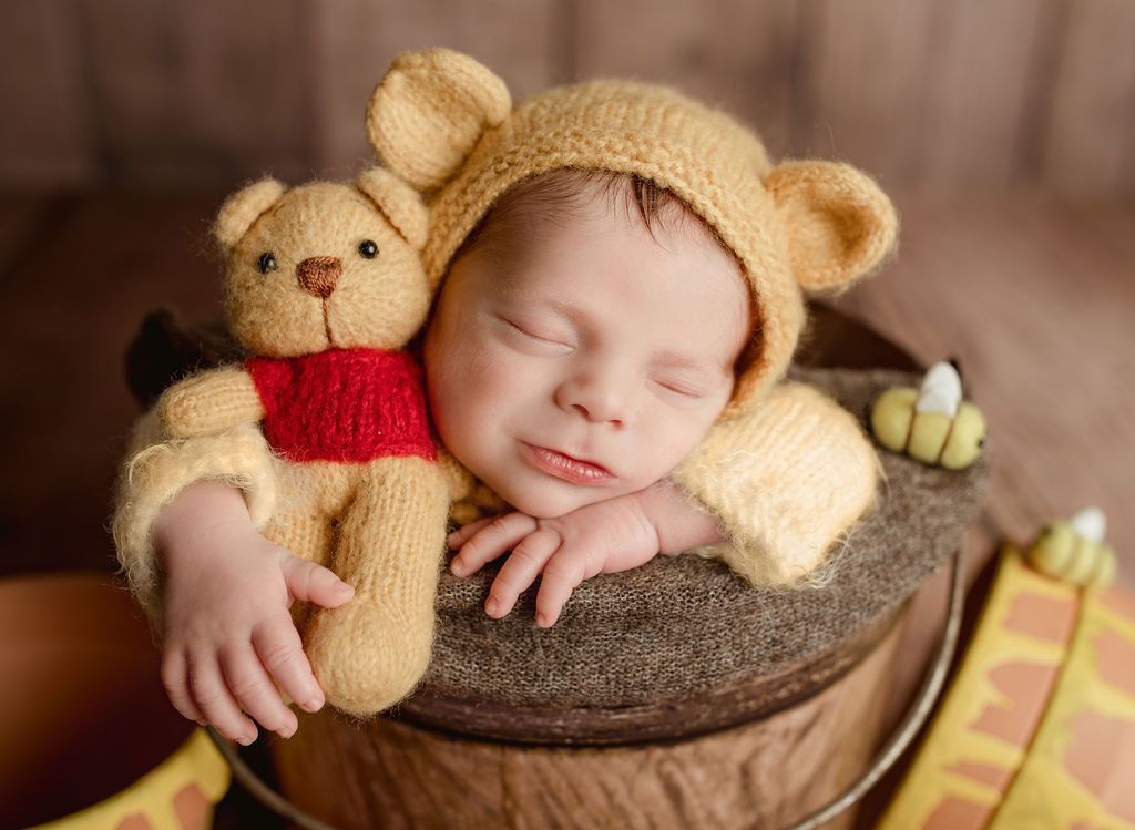 A newborn baby is wearing a winnie the pooh costume and holding a teddy bear.