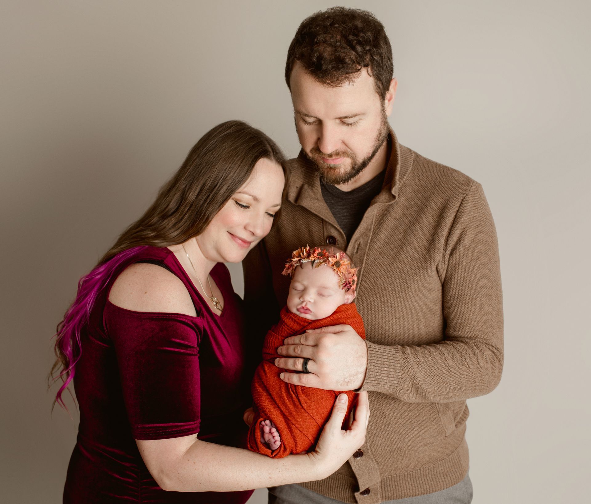 A man and woman are holding a newborn baby wrapped in a red blanket.