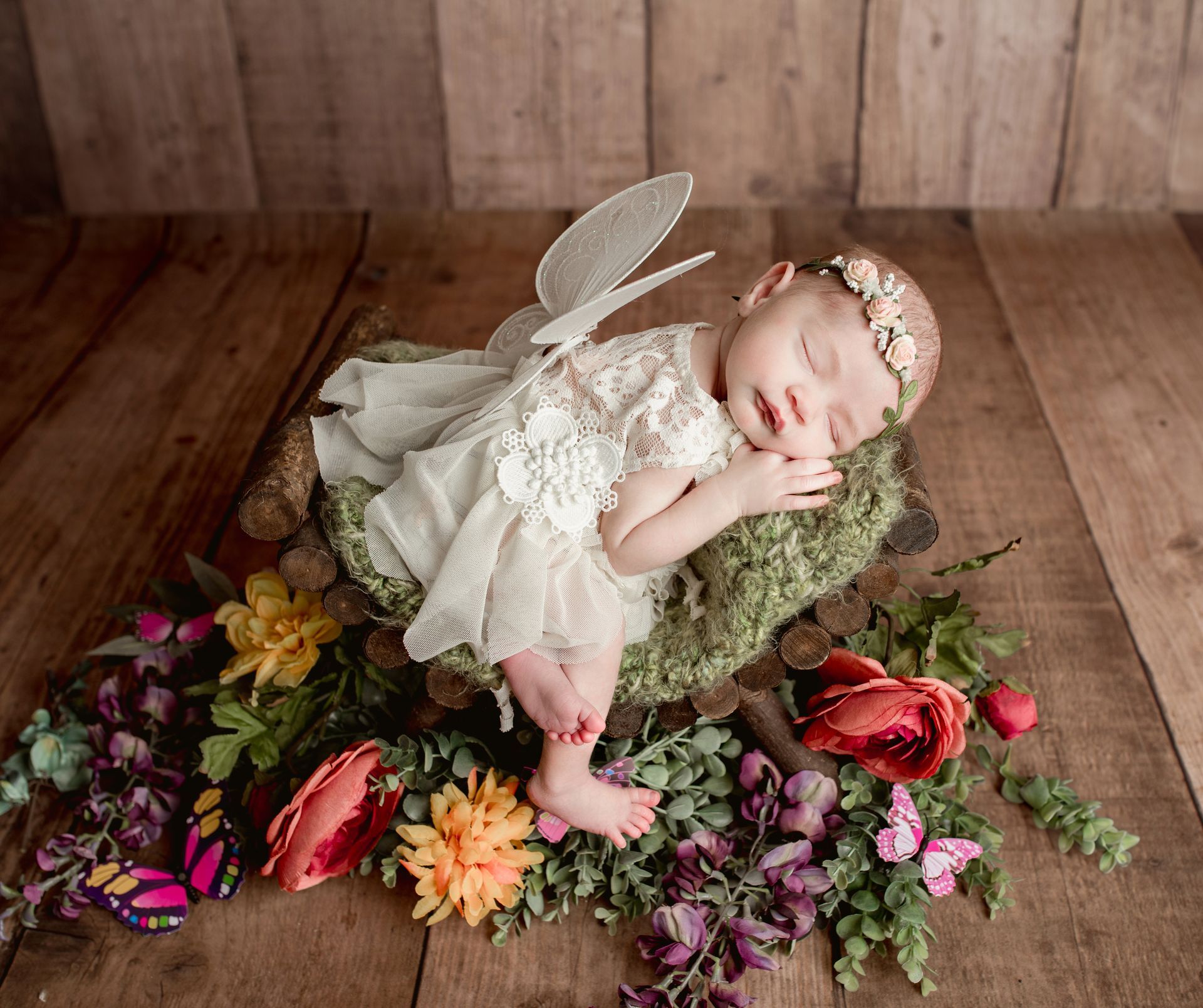 A baby in a fairy costume is sleeping on a log surrounded by flowers.