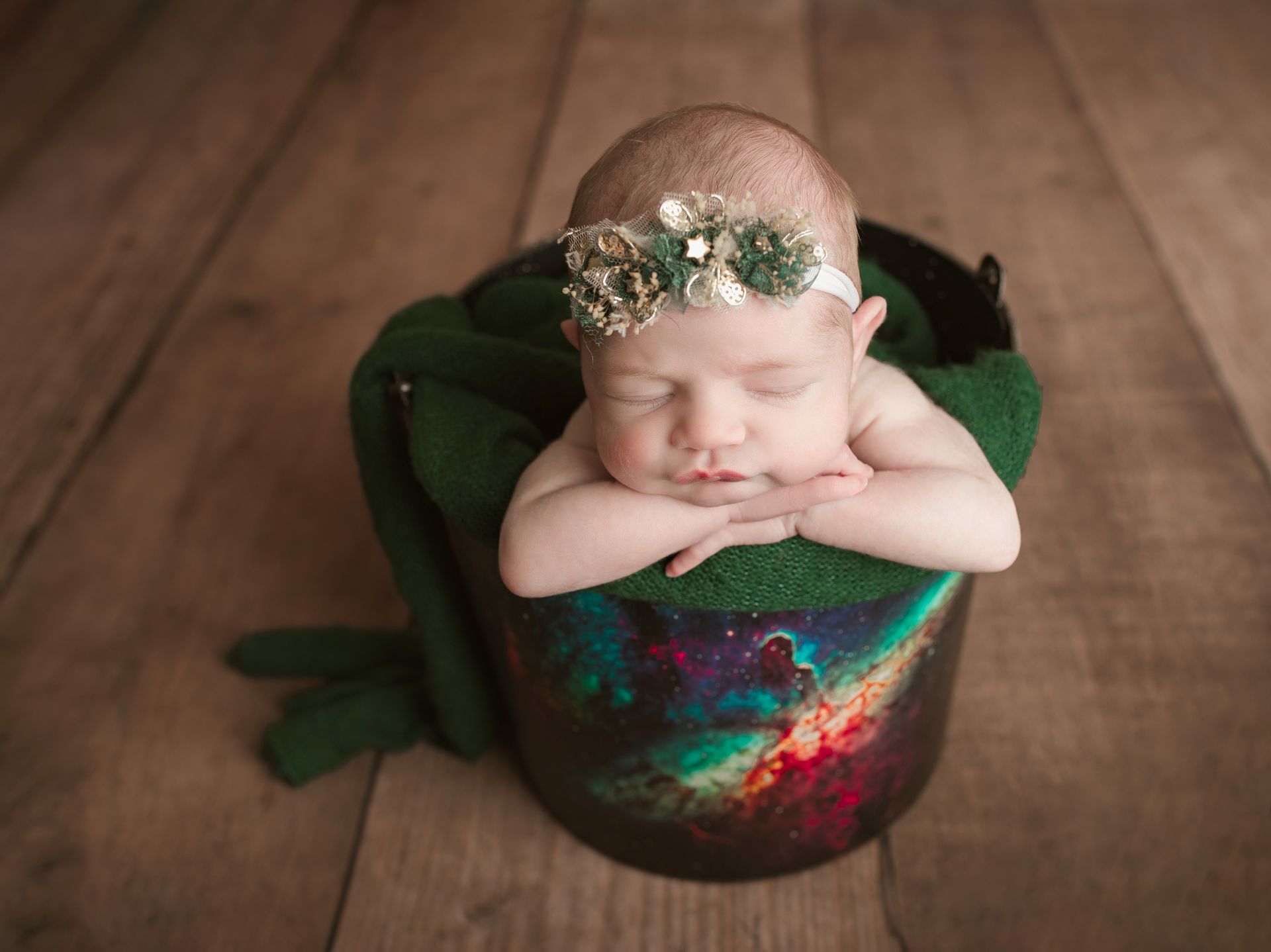 A newborn baby is sleeping in a bucket on a wooden floor.