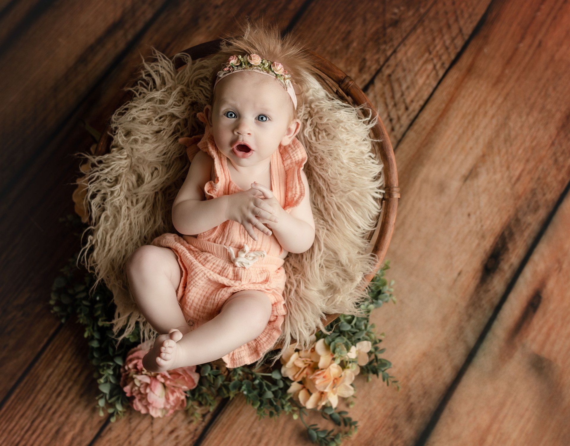 A baby girl is laying in a basket on a wooden floor.