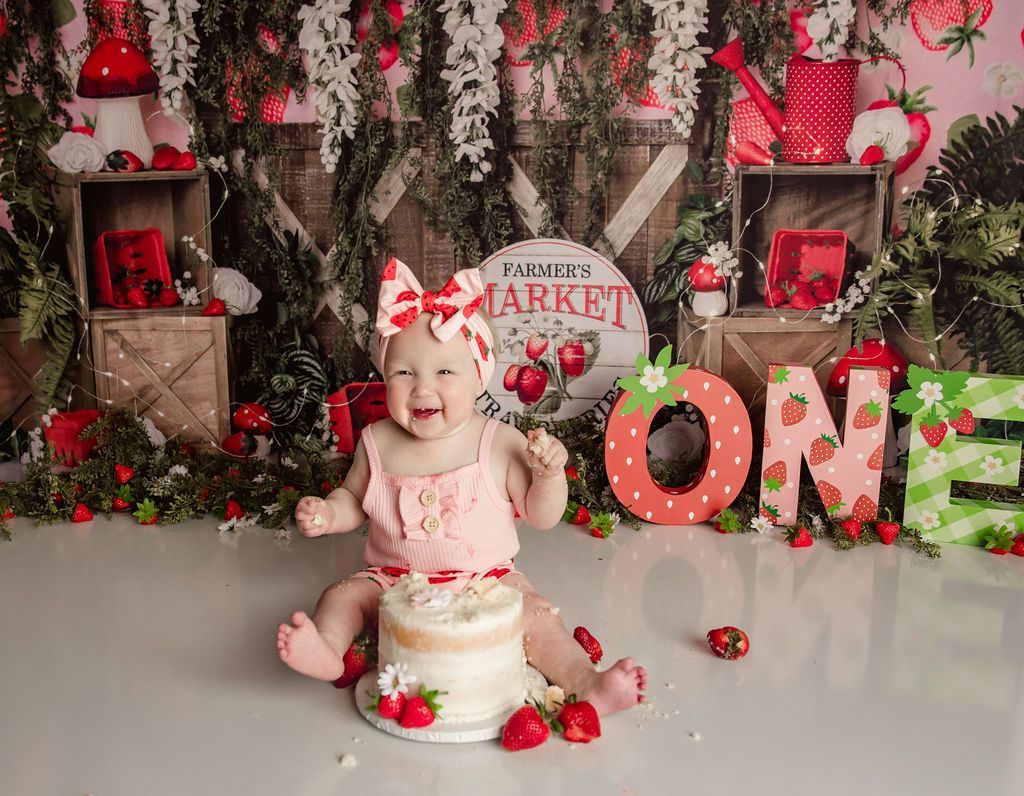 A baby is sitting in front of a cake with strawberries on it.