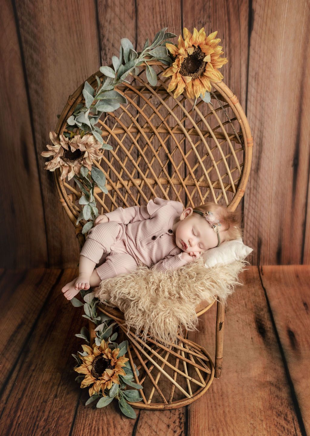 A baby is sleeping in a wicker chair decorated with sunflowers.