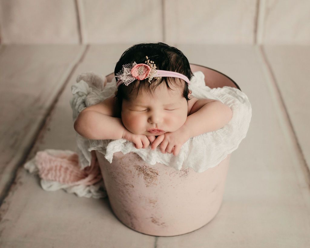 A newborn baby girl is sleeping in a pink bucket.