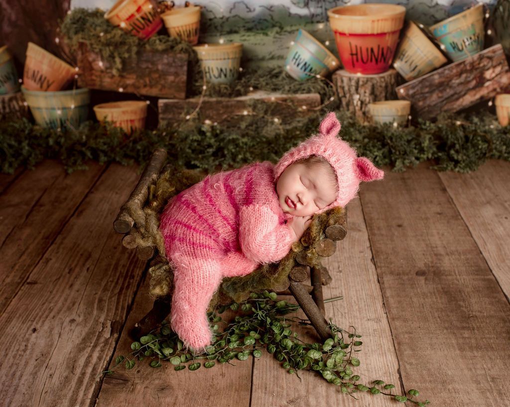 A baby in a pig costume is sleeping on a wooden floor.