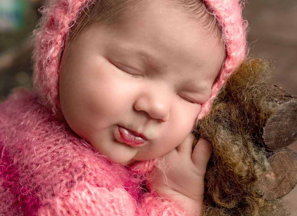A baby in a pink sweater is sleeping next to a teddy bear.