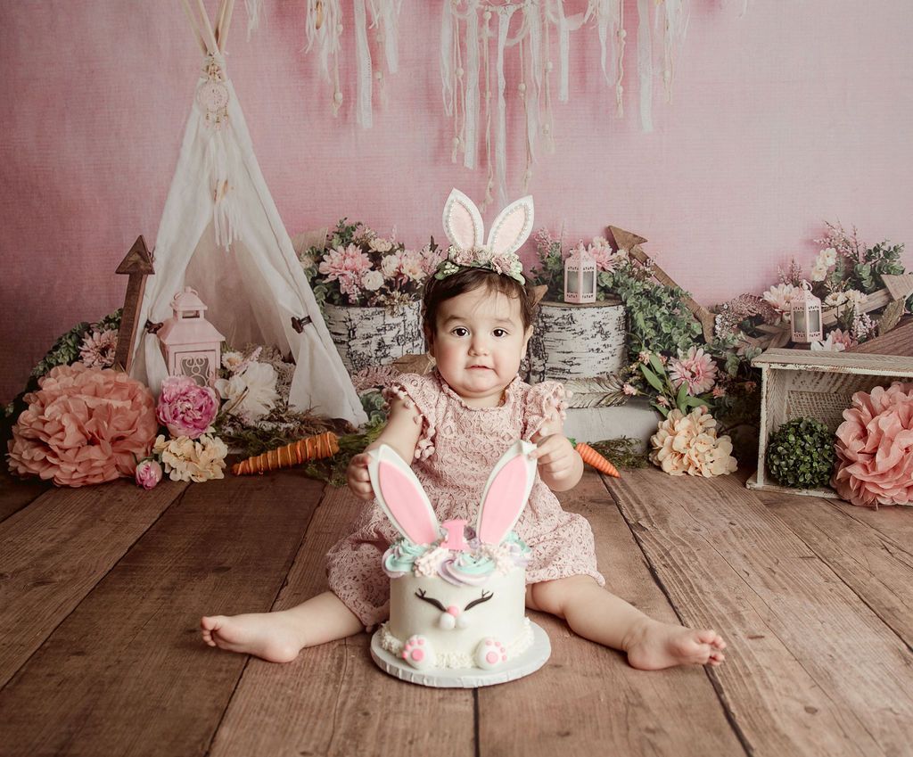 A baby girl is sitting on a wooden floor holding a cake.