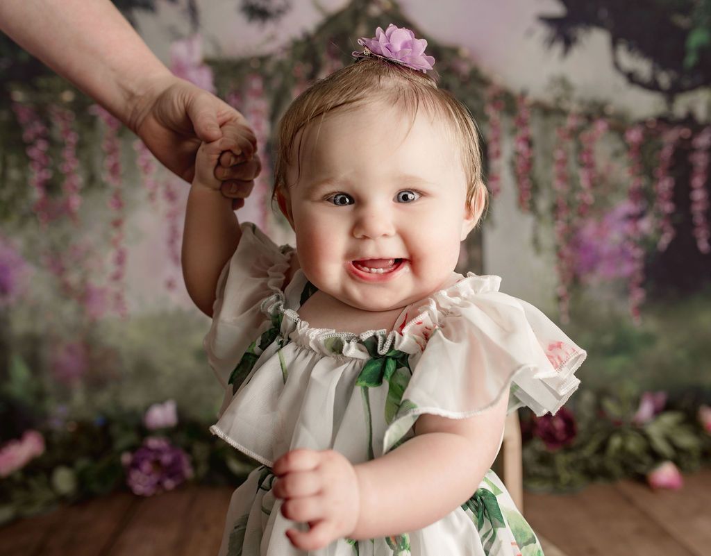 A baby girl is holding a woman 's hand and smiling.