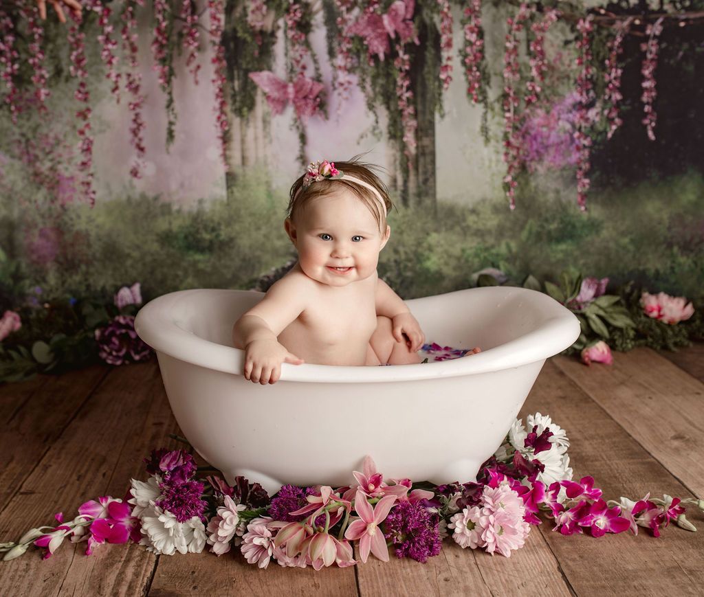 A baby is sitting in a bathtub surrounded by flowers.
