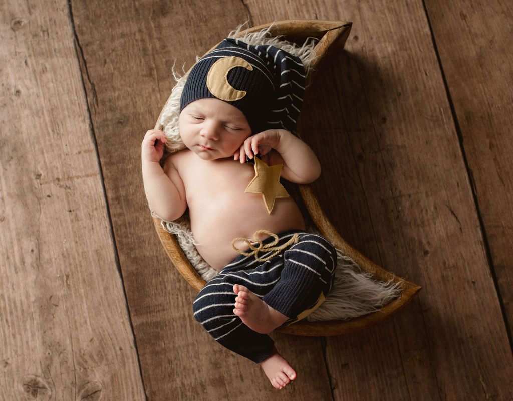 A newborn baby is sleeping in a basket on a wooden floor. Oregon newborn photographer near me