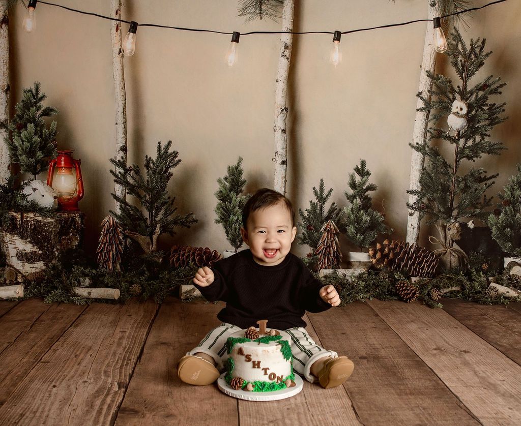 A baby is sitting on a wooden floor next to a cake.