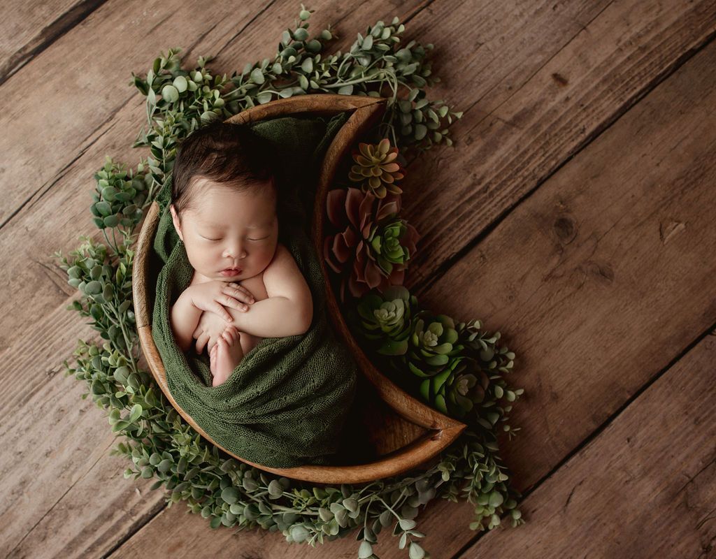 A newborn baby is wrapped in a green blanket and sleeping in a crescent moon.