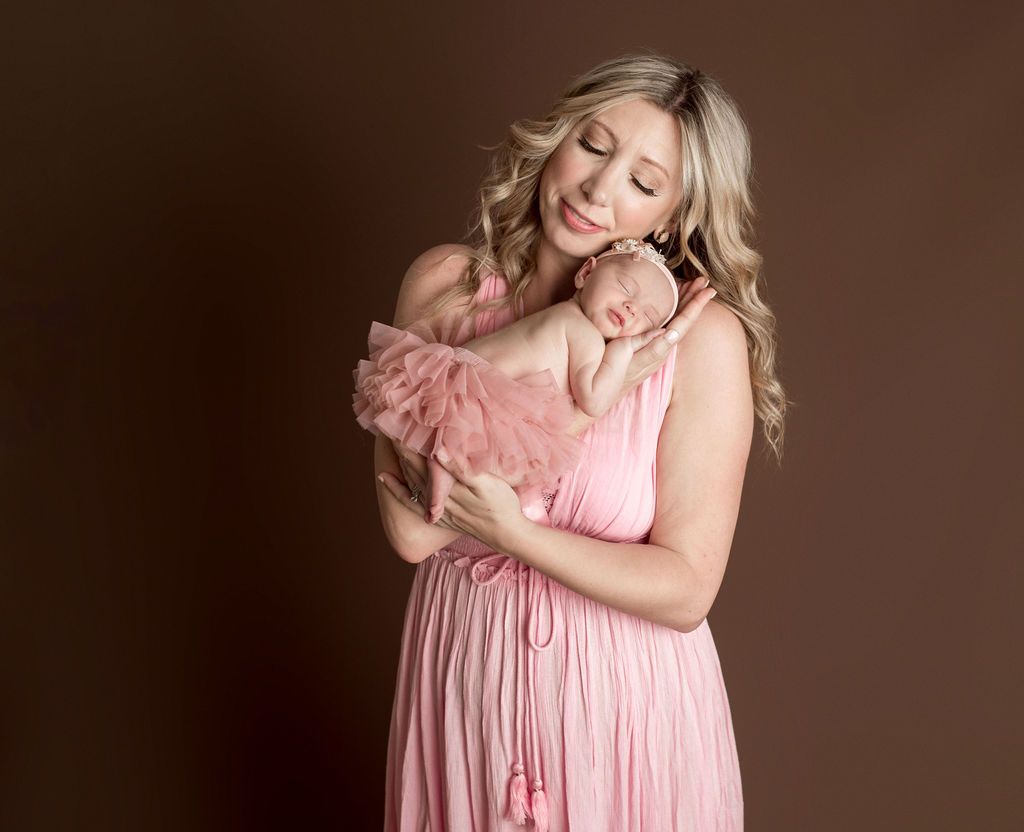 A woman in a pink dress is holding a newborn baby in her arms.