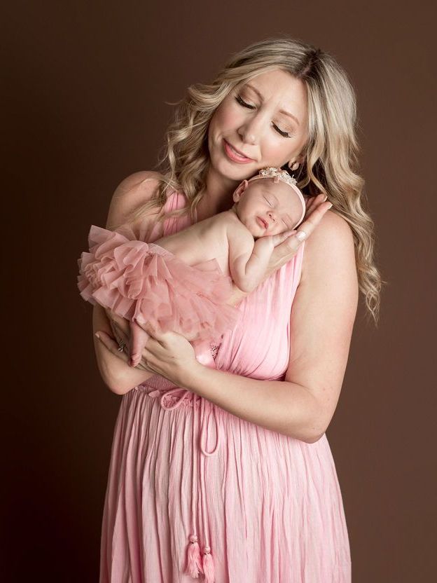 A woman in a pink dress is holding a newborn baby in her arms.
