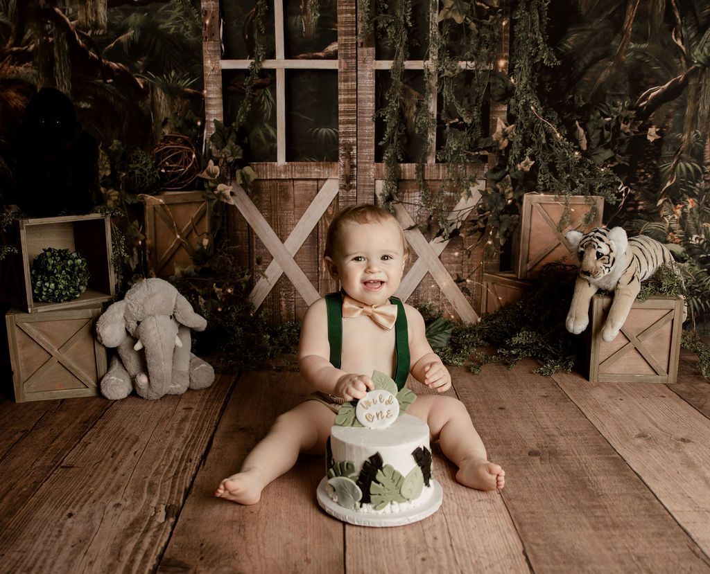 A baby is sitting on a wooden floor next to a cake.