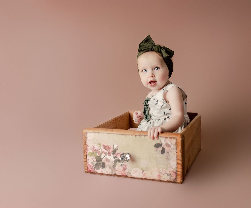 A baby girl is sitting in a wooden drawer.