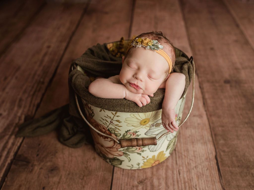A newborn baby is sleeping in a bucket on a wooden floor. Newborn studio with props
