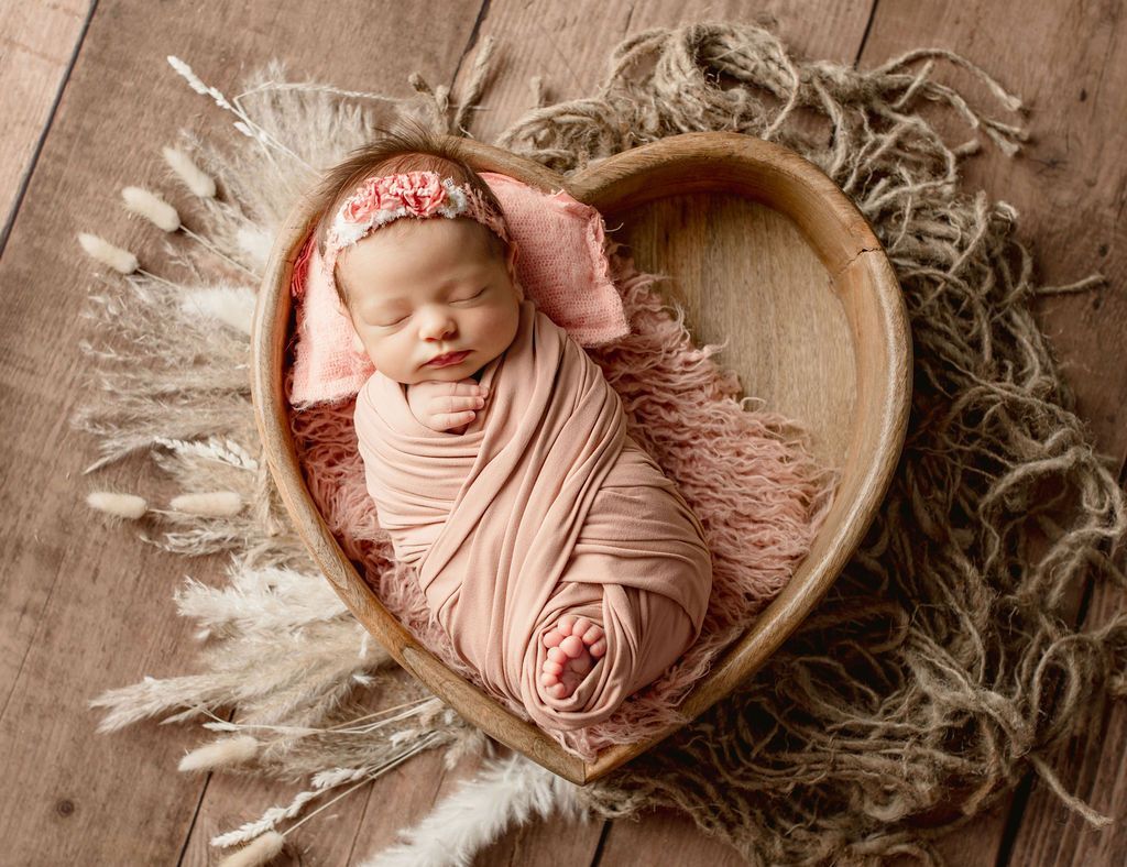 A newborn baby is sleeping in a heart shaped wooden bowl.
