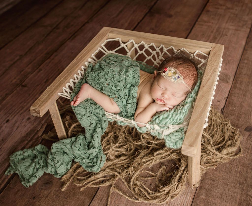 A newborn baby is sleeping in a wooden hammock. Newborn studio with props