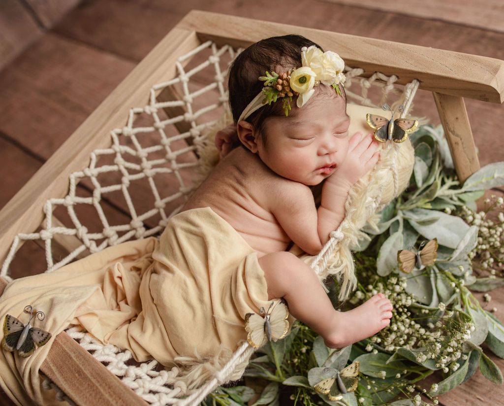 A newborn baby is sleeping in a hammock with flowers on it.