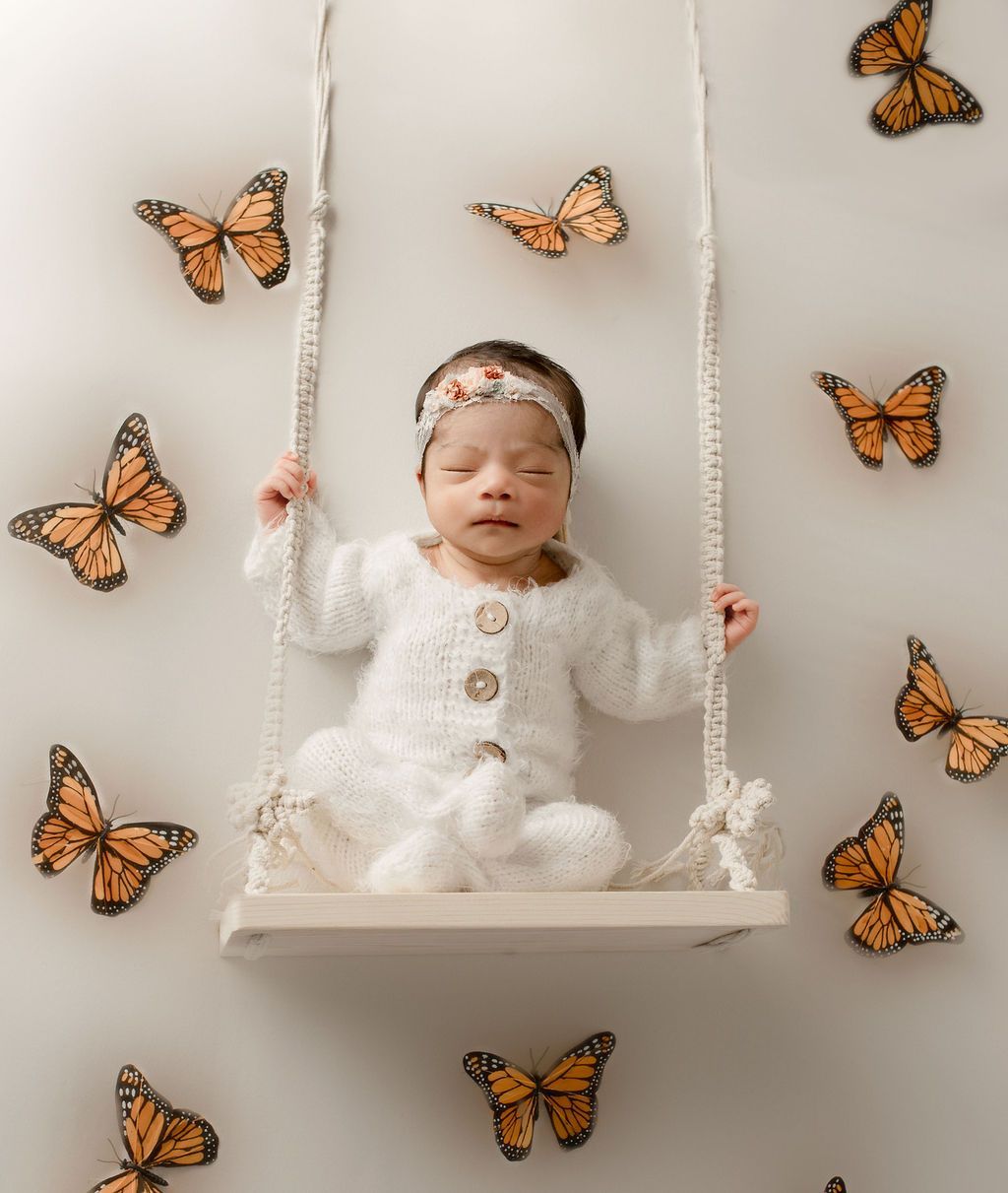 A baby is sitting on a swing surrounded by butterflies