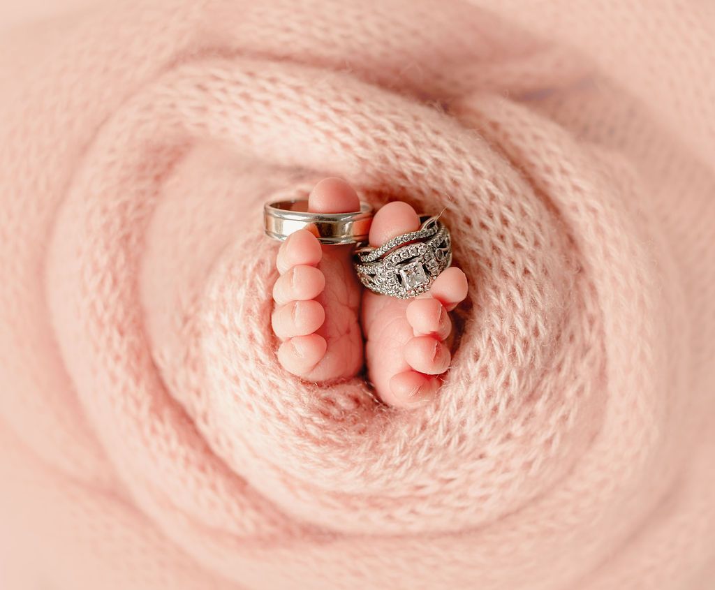 A baby 's feet with wedding rings on them are wrapped in a pink blanket.