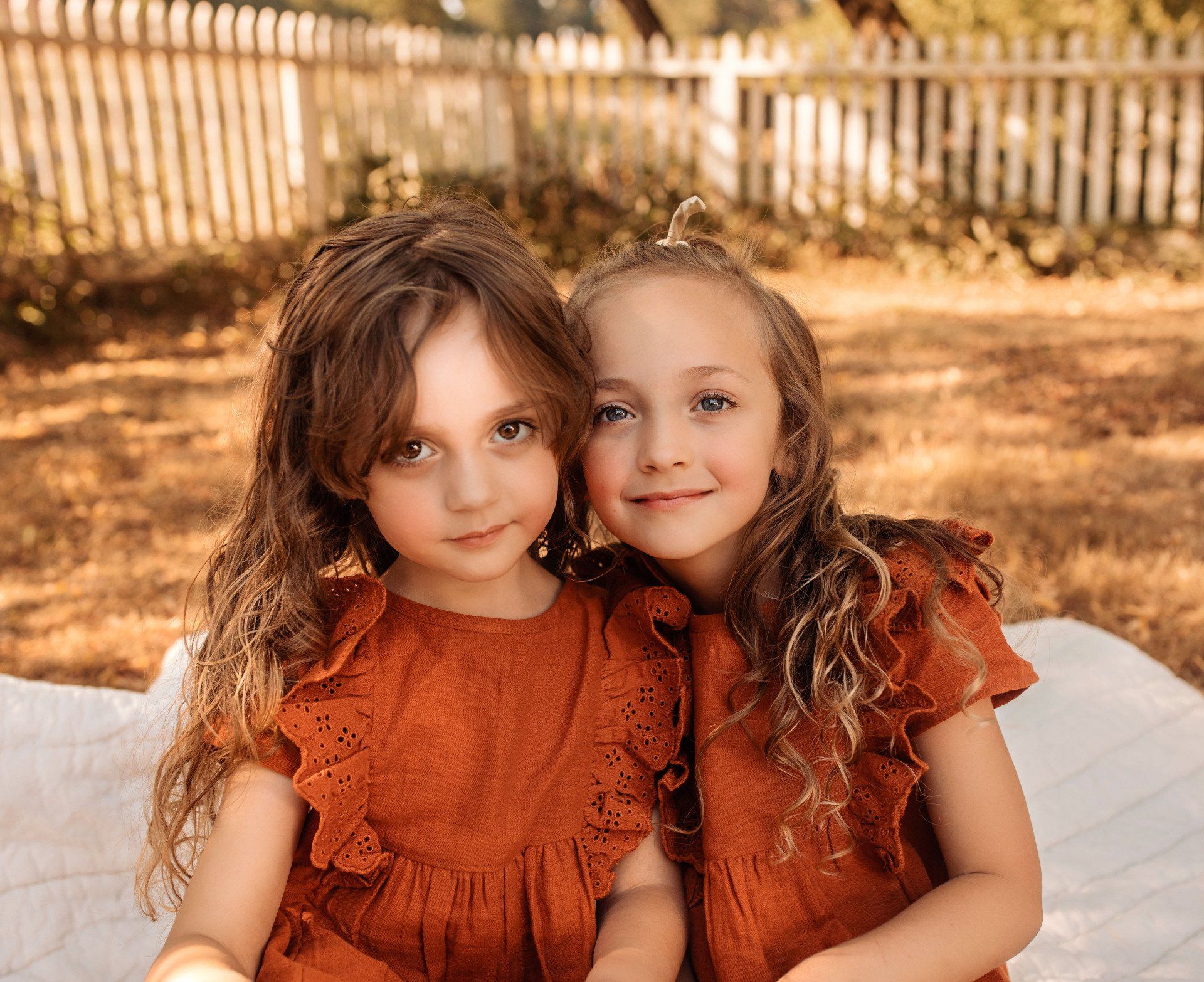 Two little girls are sitting next to each other on a blanket.