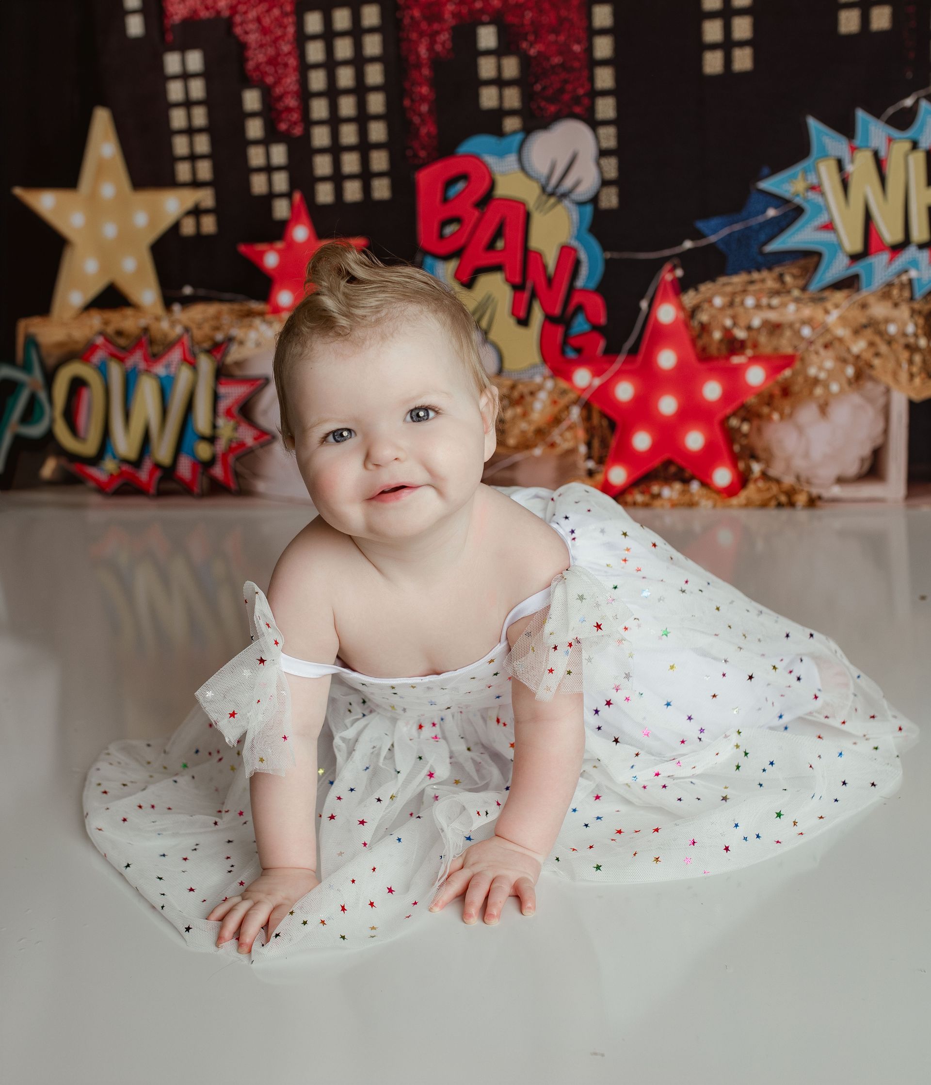 A baby in a white dress is crawling on the floor.