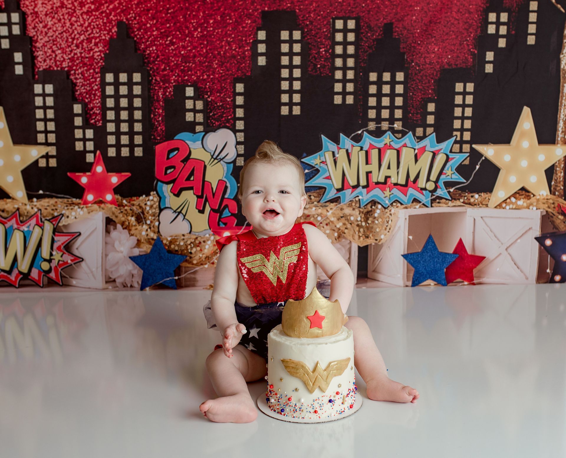 A baby is sitting on top of a wonder woman cake.