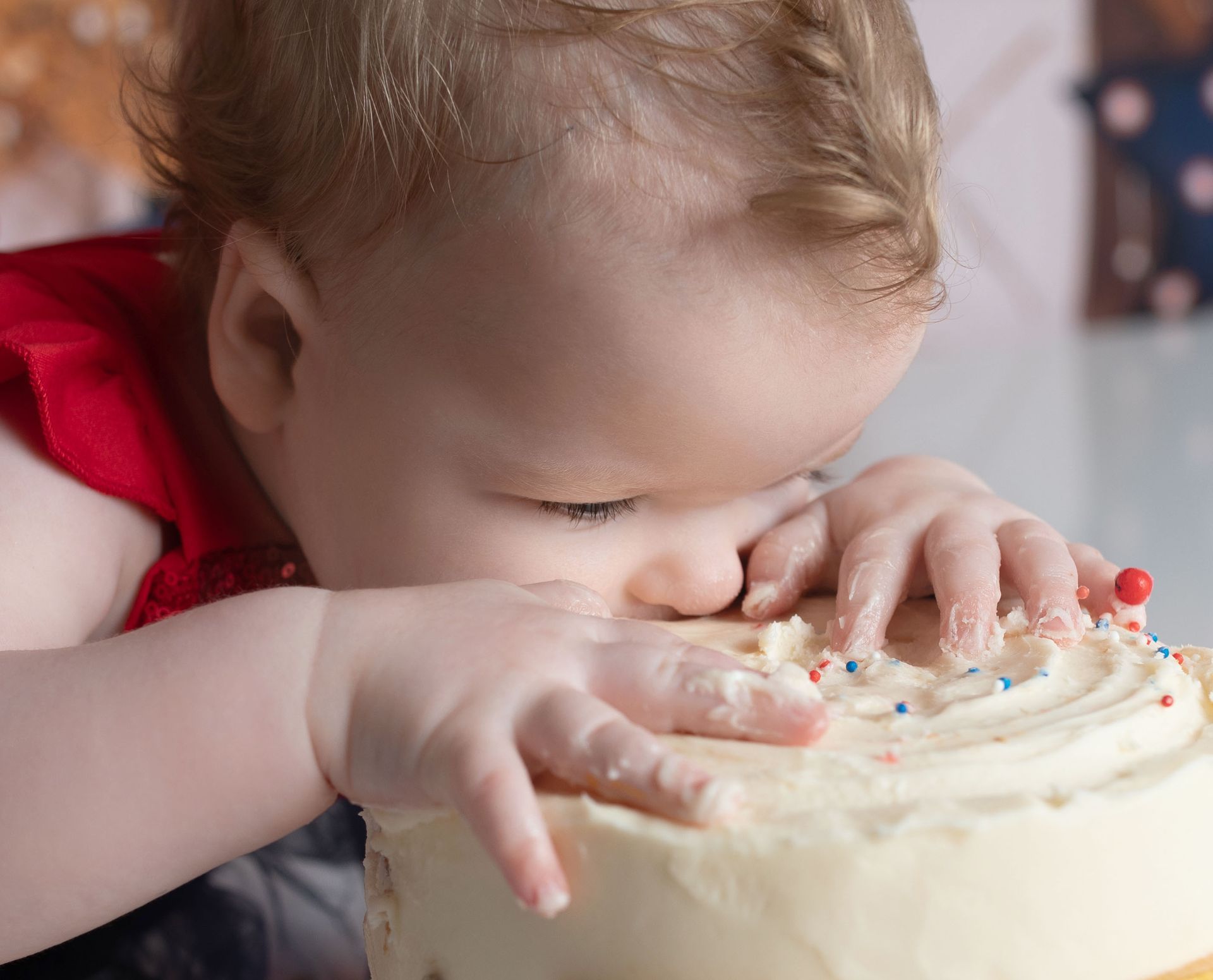 A baby is eating a cake with frosting and sprinkles on it.